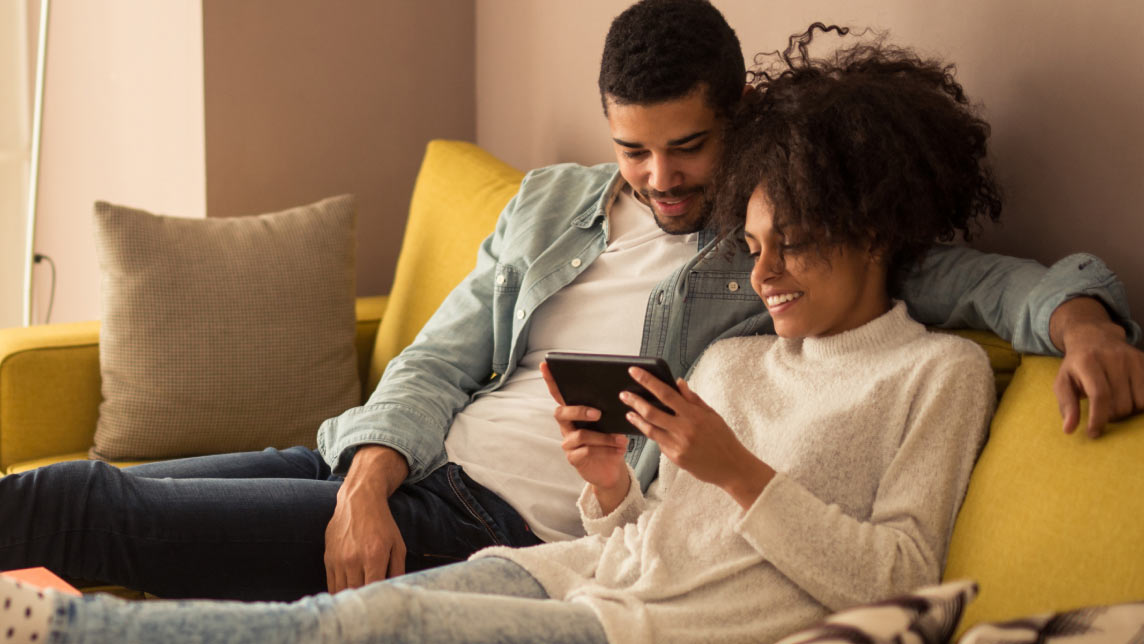 A couple sitting on a sofa viewing a 3D Tour on a smartphone